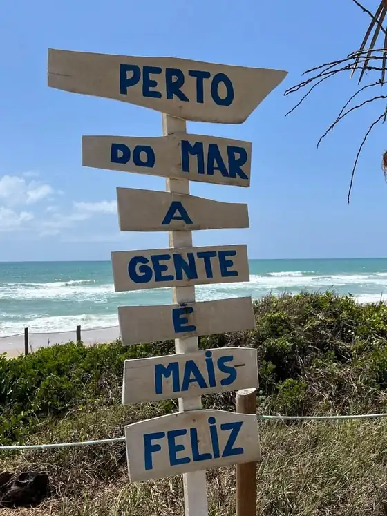 Placa de madeira na praia com a frase Perto do mar a gente é mais feliz